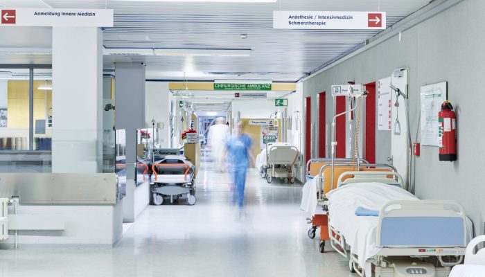 Flur im Krankenhaus mit unscharfem Arzt in Bewegung und Lift rot und Bett
